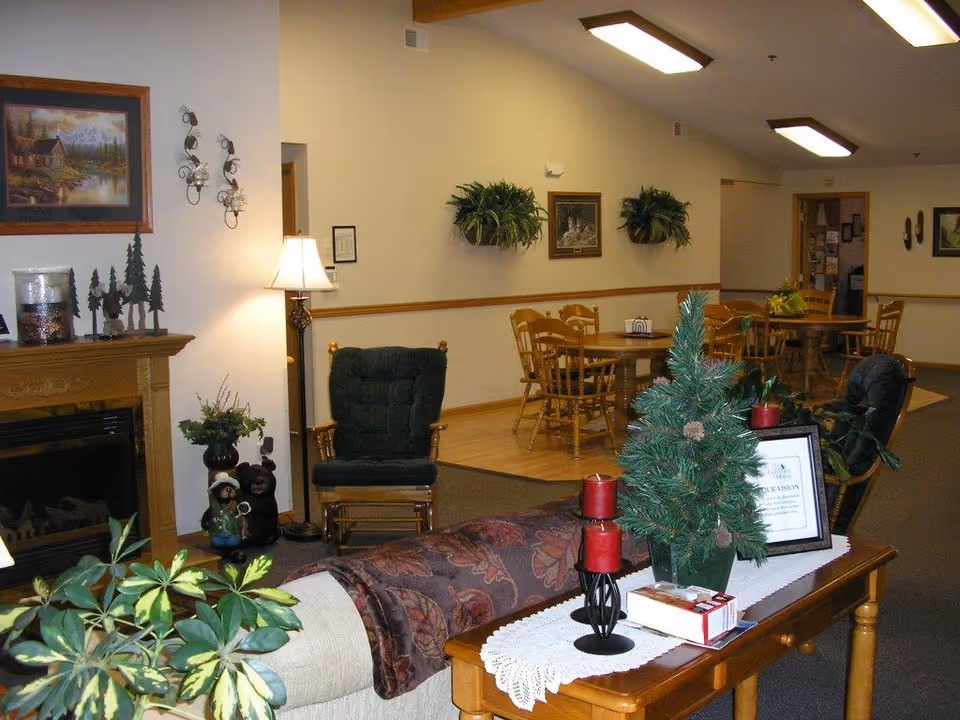 Community living room with seating, a fireplace, dining tables in the background, and holiday decorations on a console table.