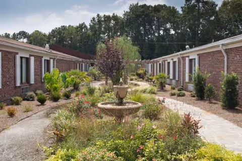 Brick senior housing courtyard with a central fountain and landscaped garden beds.
