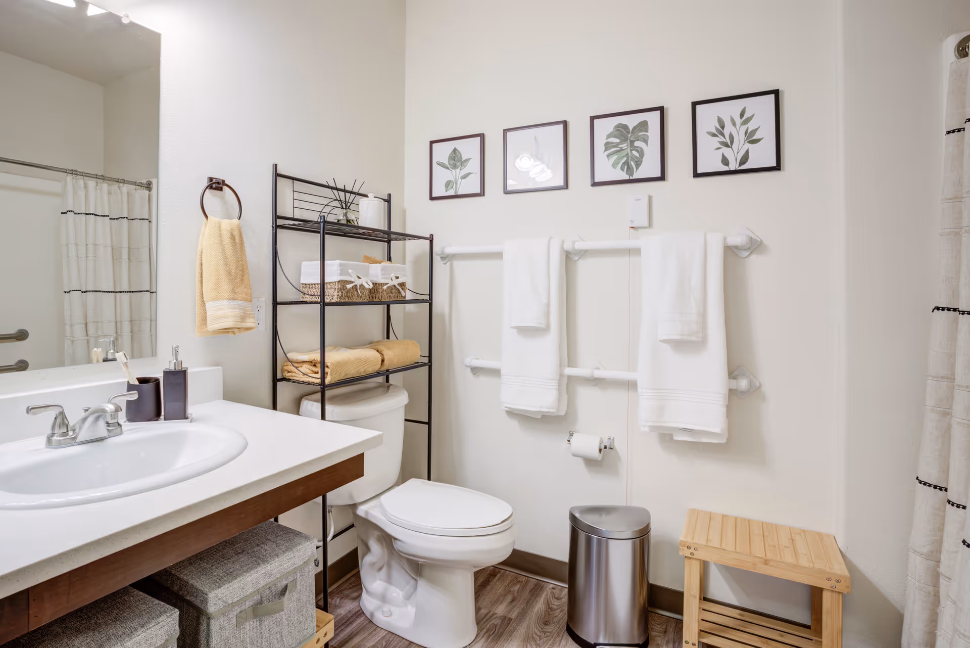 Clean, well-lit bathroom with a sink and vanity, toilet with shelving above, and towels hanging on wall bars.