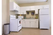Small kitchenette with white cabinets, a stove, refrigerator, sink, and paper towel dispenser.