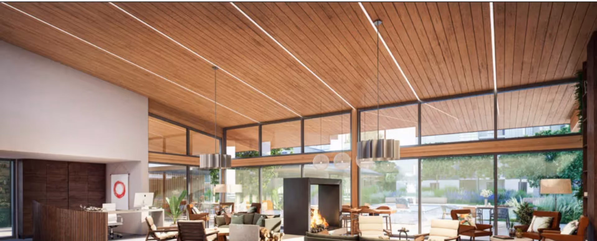 Spacious and modern interior of a senior living facility with a high wooden ceiling, large floor-to-ceiling windows, multiple seating areas with chairs and tables, a fireplace in the center, and pendant lights hanging from the ceiling. The room is bright with natural light and has a view of an outdoor garden area.