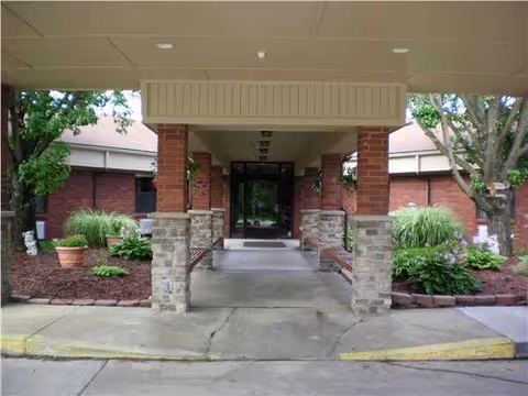 Covered entrance to a brick facility with landscaped sides and glass doors.