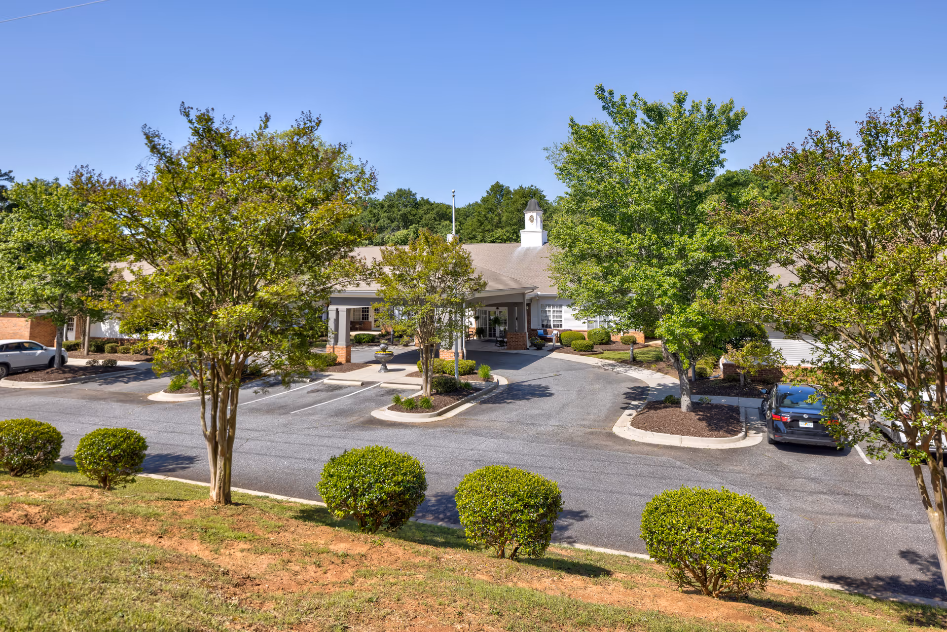 Front exterior view of TerraBella Marchbanks facility with a driveway, parking spaces, several trees, bushes, and a clear blue sky.