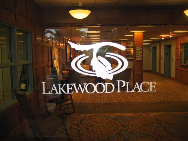 Glass entrance featuring a white 'Lakewood Place' logo with a view into the facility's carpeted lobby.