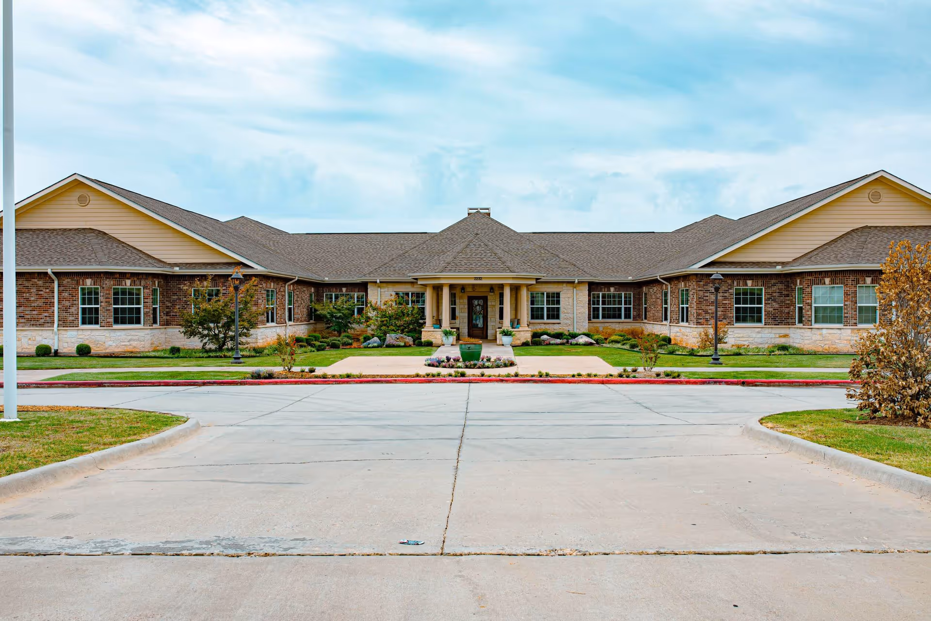 Front exterior of a single-story brick senior living building with a central entrance, driveway, and landscaped lawn.