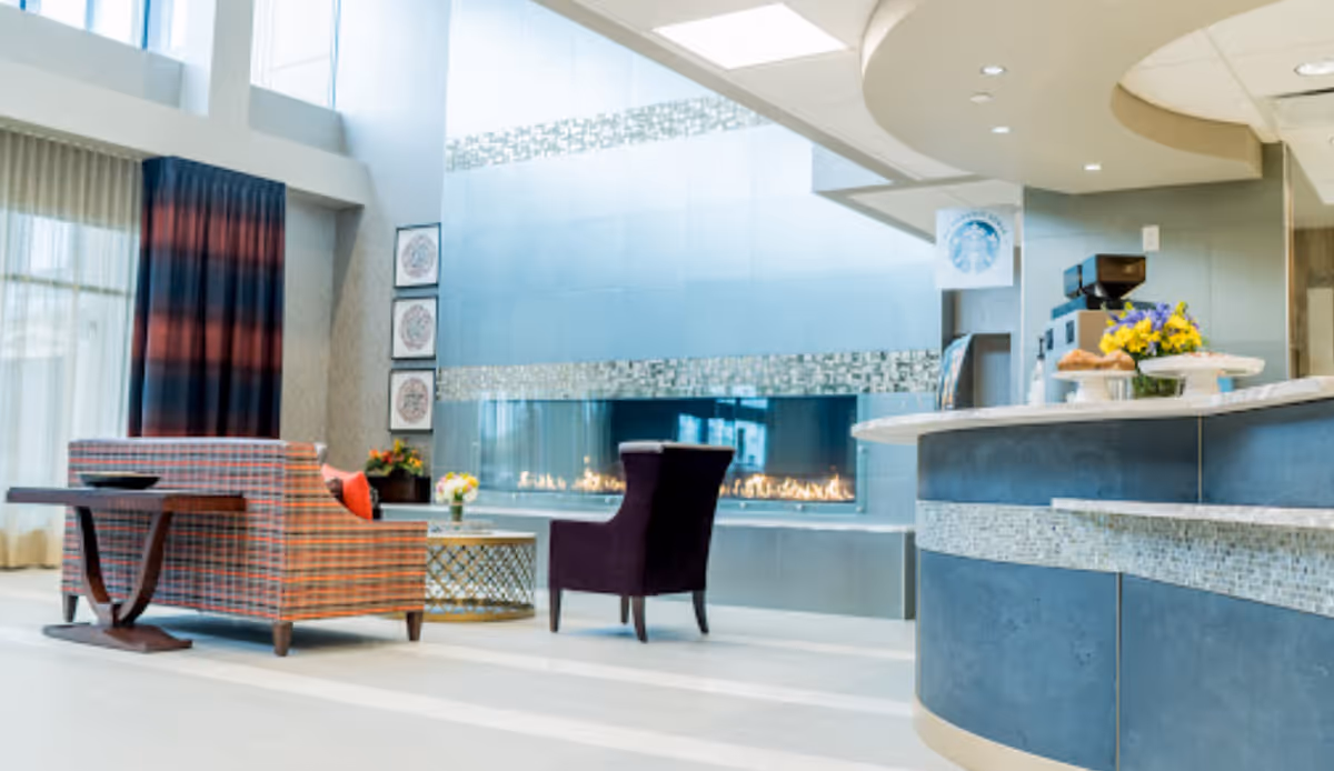 Modern senior living lobby with blue walls, fireplace, curved reception desk, and colorful seating.