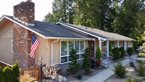 Exterior of a single-story senior living facility with flag and landscaped walkway.