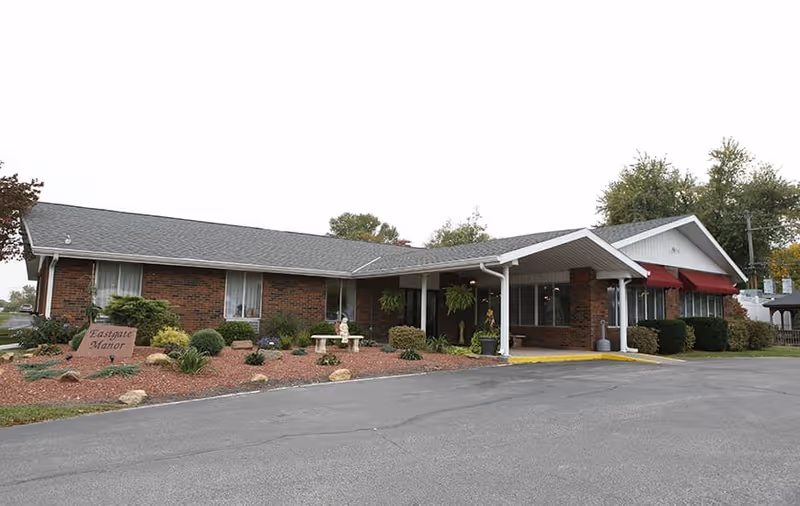 Single-story brick nursing facility with a covered entrance, landscaped beds and a sign reading "Eastgate Manor".
