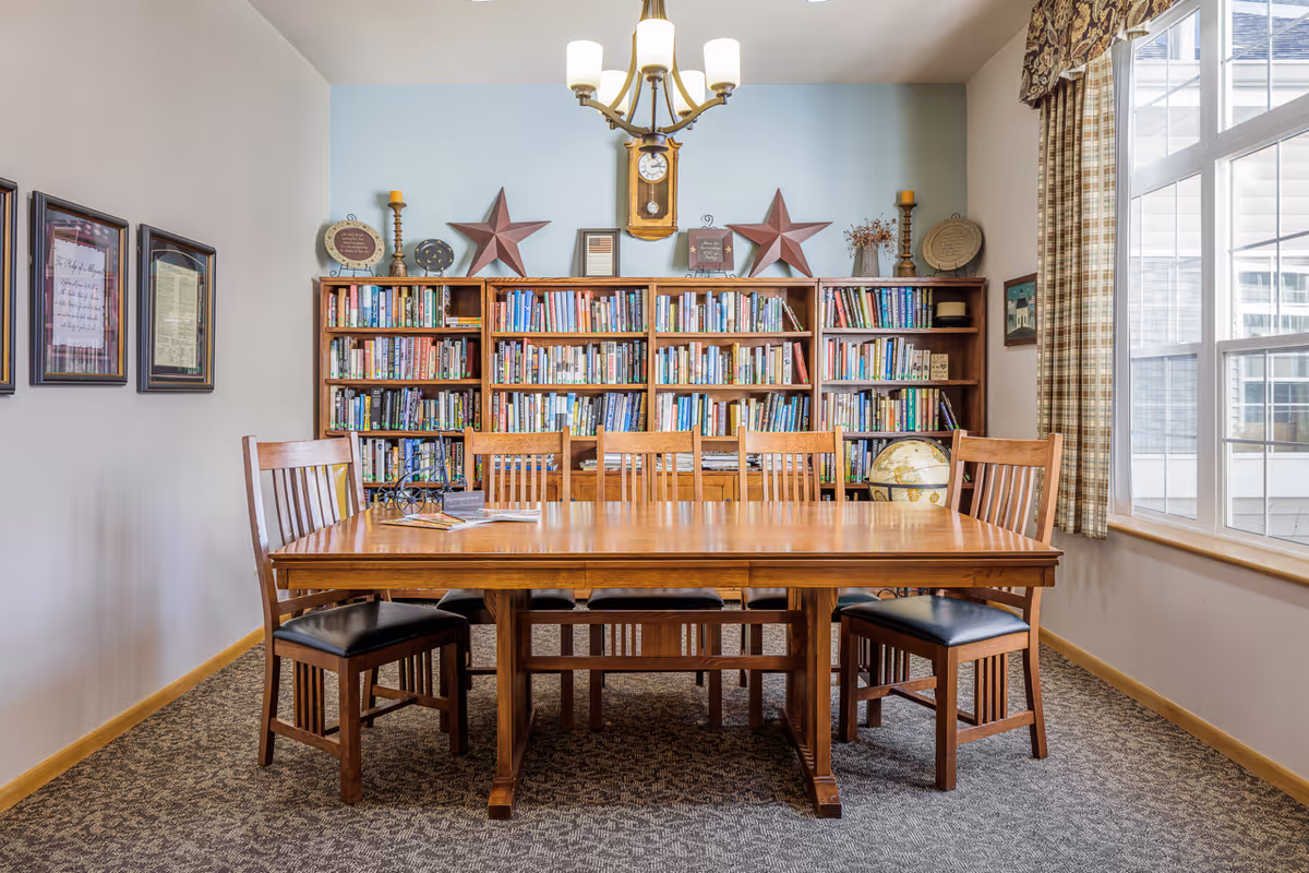 Wooden table and chairs in a well-lit common room with bookshelves, a globe, and a large window.