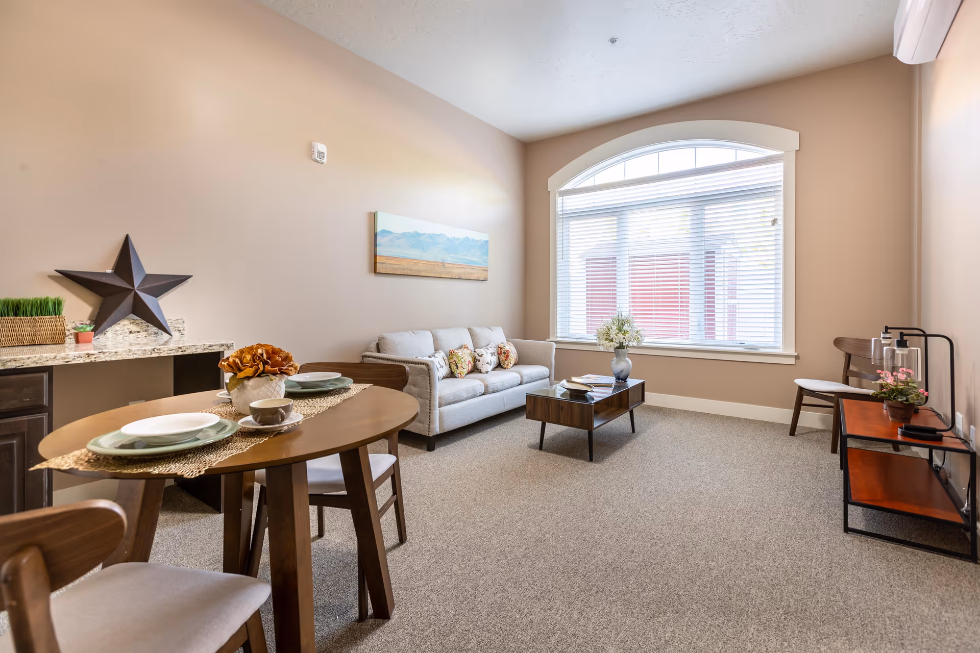 Bright living room with a small dining table, sofa, coffee table and a large arched window.