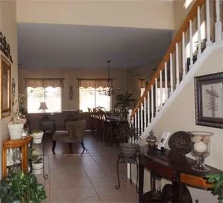 Spacious senior living common area with seating, plants, and a staircase to an upper level.