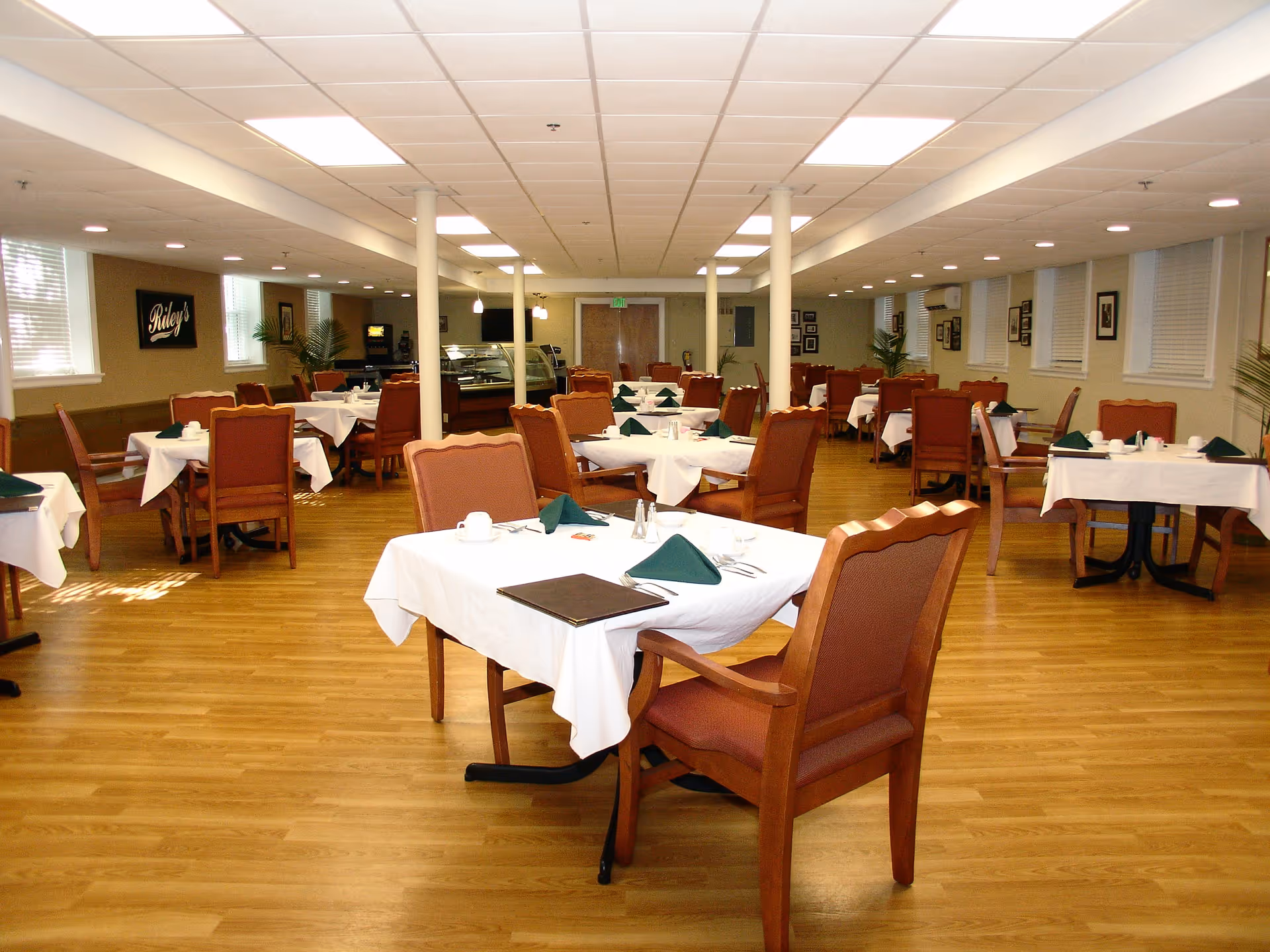 Spacious dining room with multiple tables set with white linens and wooden chairs on a hardwood floor.