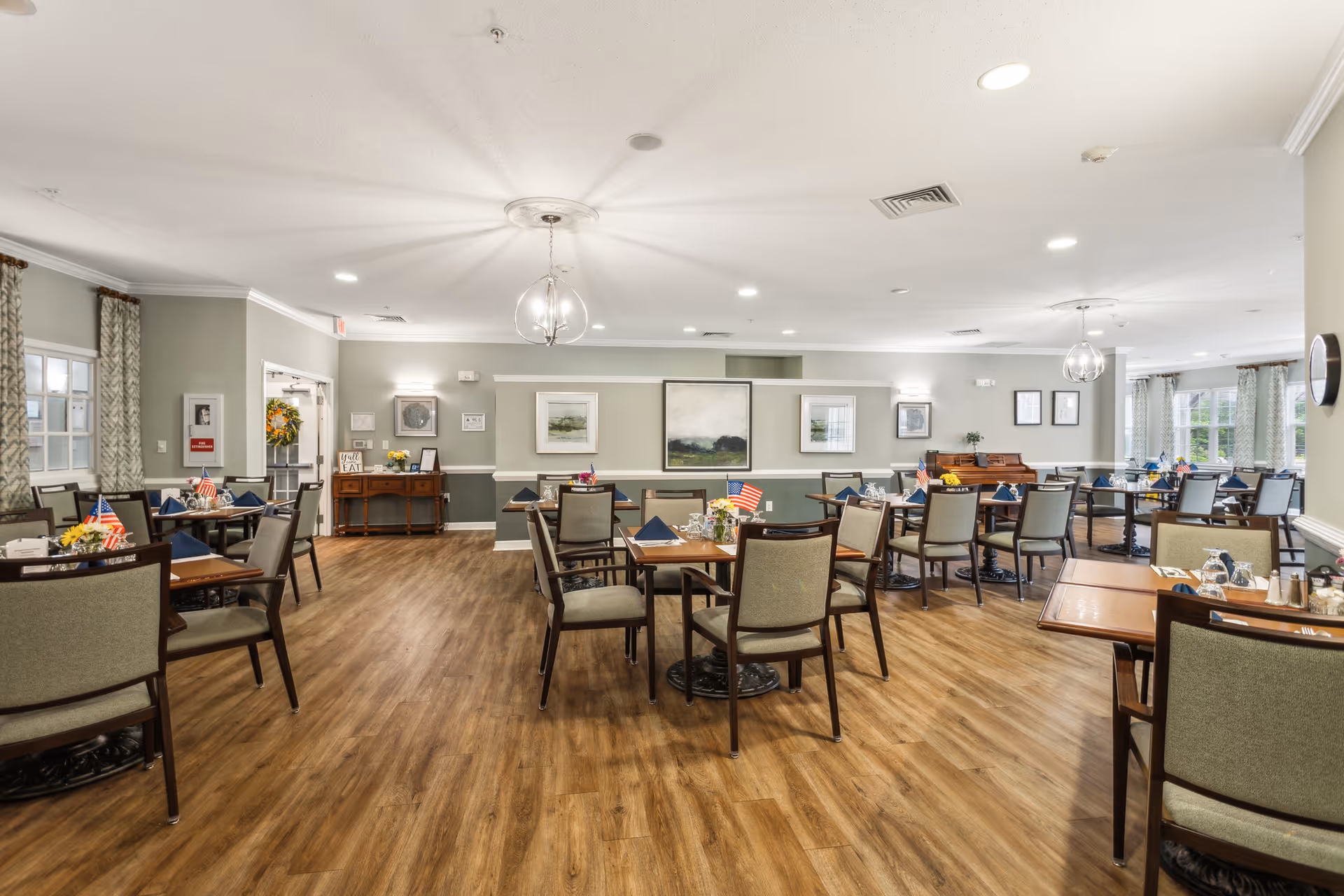 Spacious, well-lit dining room with multiple set tables and chairs, wood flooring, and neutral decor.
