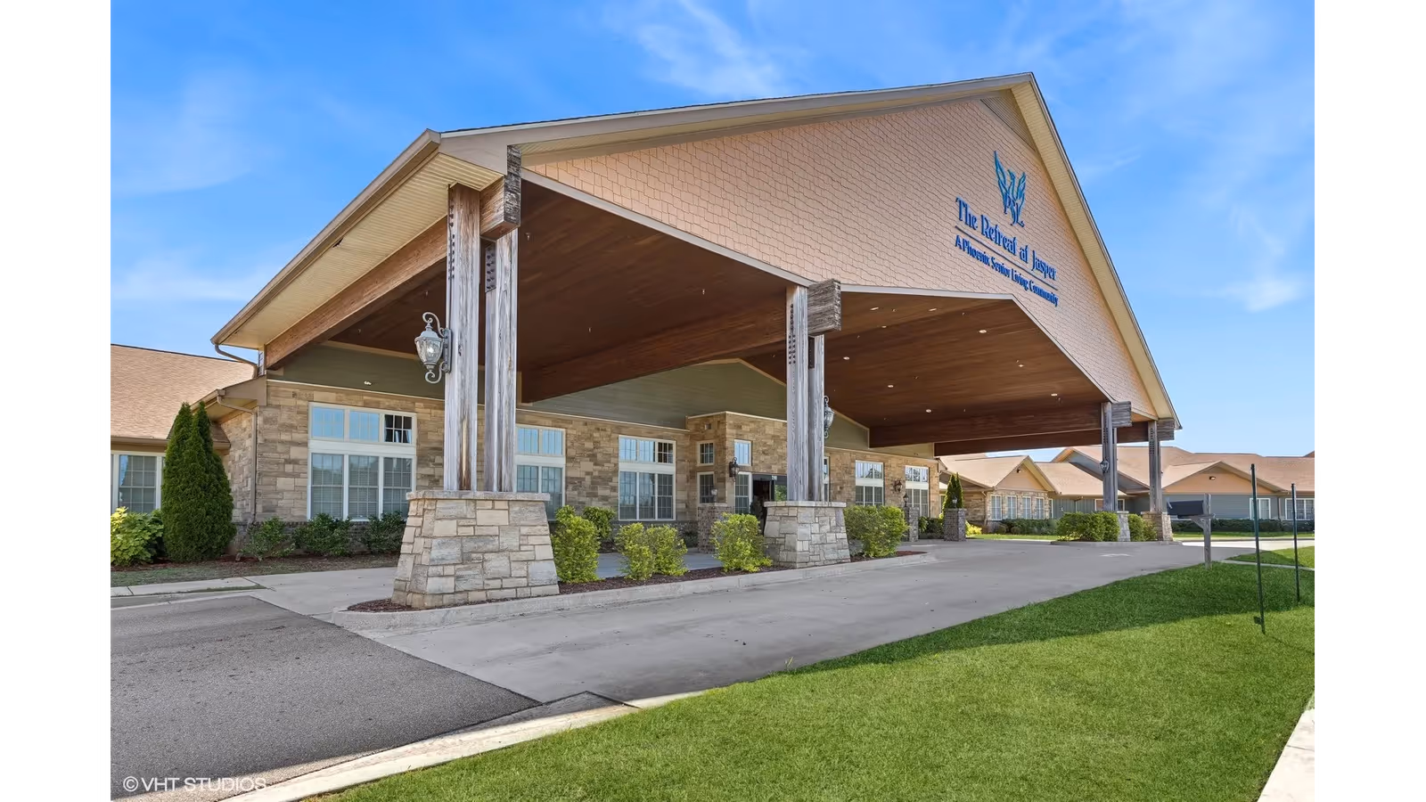 Covered porte-cochere entrance of The Retreat at Jasper senior living building with stone pillars and landscaped grounds.