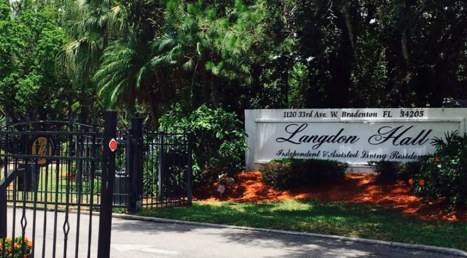 Entrance gate and sign for Langdon Hall Independent & Assisted Living Residence surrounded by greenery and trees.