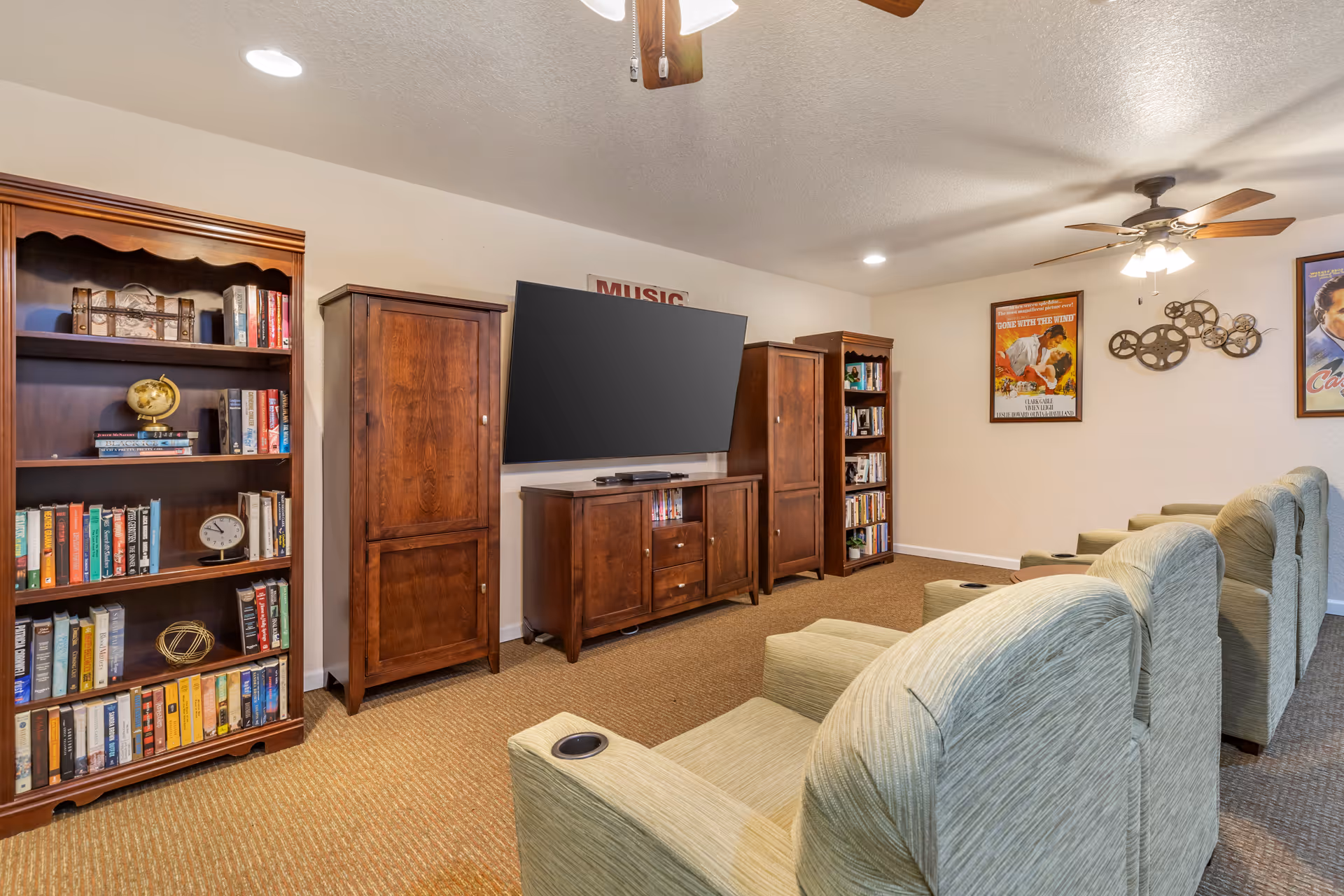 Cozy media room with reclining chairs facing a wall-mounted TV, flanked by wooden cabinets and bookcases.