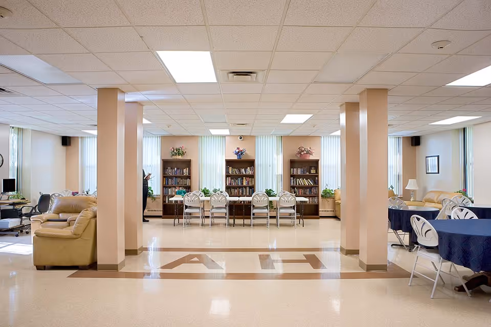 Spacious common room with bookshelves along the far wall, rows of chairs and tables, and seating areas with sofas.
