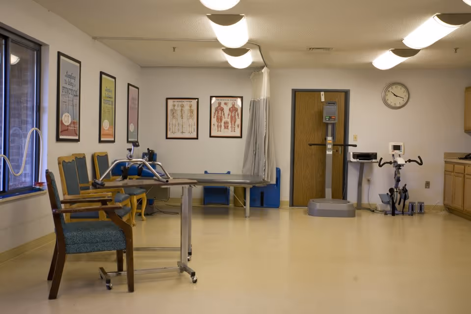 Physical therapy/rehab room with chairs, a treatment table, exercise equipment and anatomy charts on the walls.