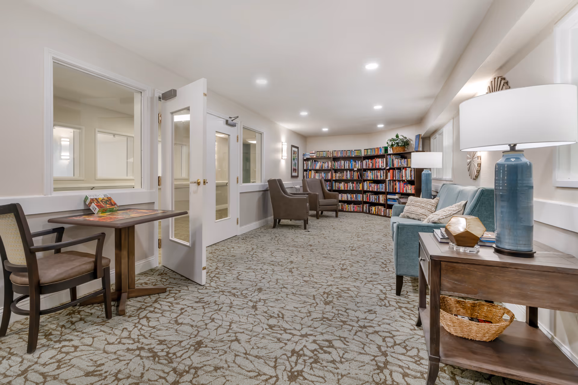 Well-lit lounge/library with bookshelves, armchairs, a sofa, side tables and lamps.