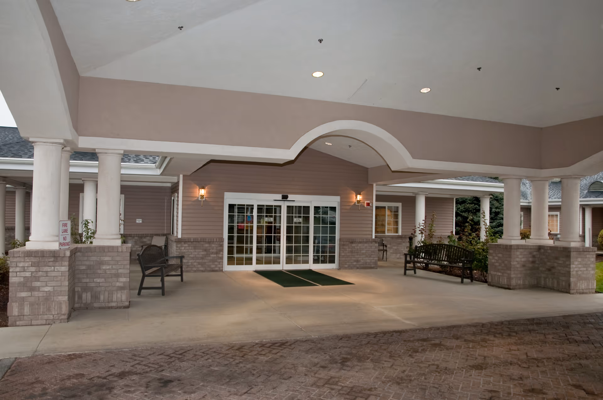Covered driveway and main entrance with columns, benches, and sliding glass doors.