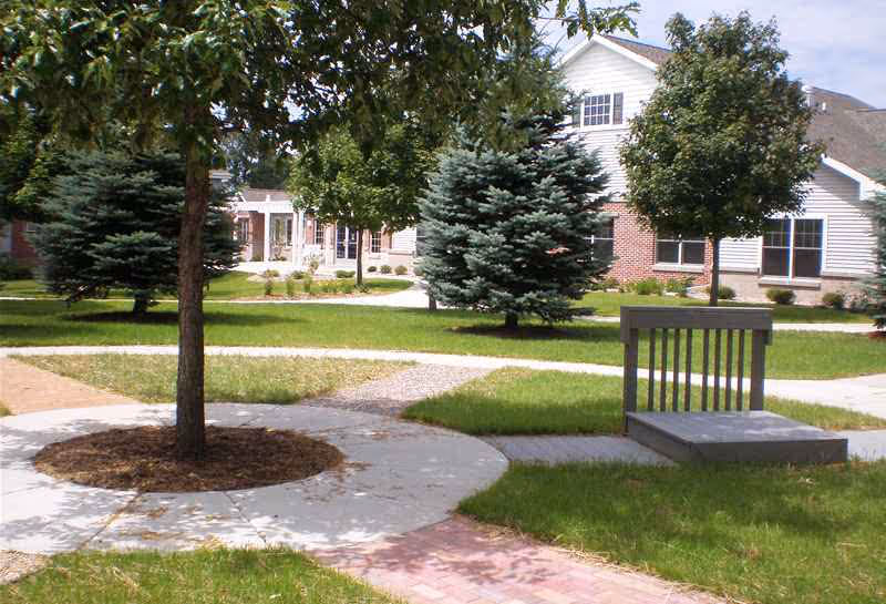 Exterior view of Rennes Health and Rehab Center courtyard with trees, paths, and seating.