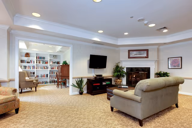 Spacious lounge with a sofa facing a wall-mounted TV and fireplace, and an adjacent library visible through an open doorway.