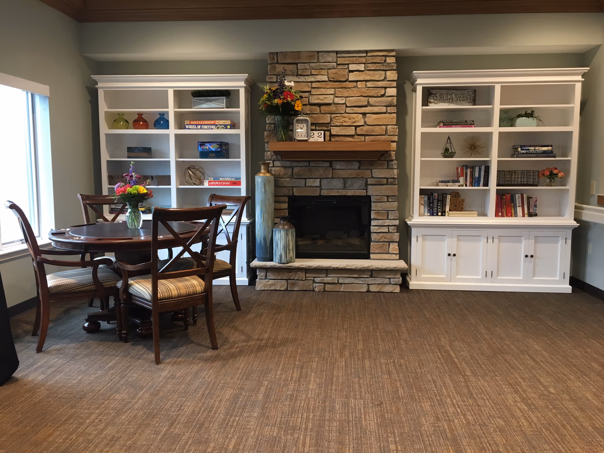 Cozy common room with a stone fireplace flanked by white built-in bookshelves and a round wooden table with four chairs.