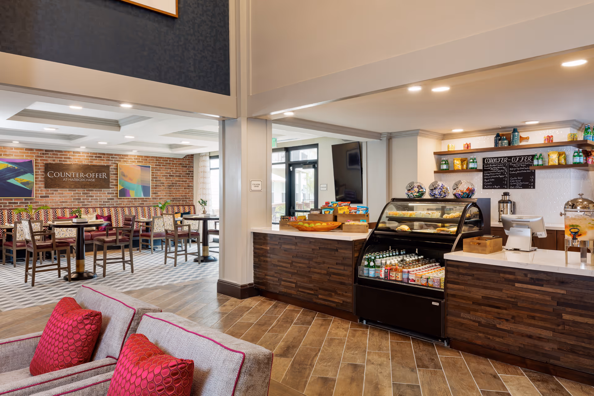 Open communal dining and café area with seating, a service counter and refrigerated display in a senior living facility.