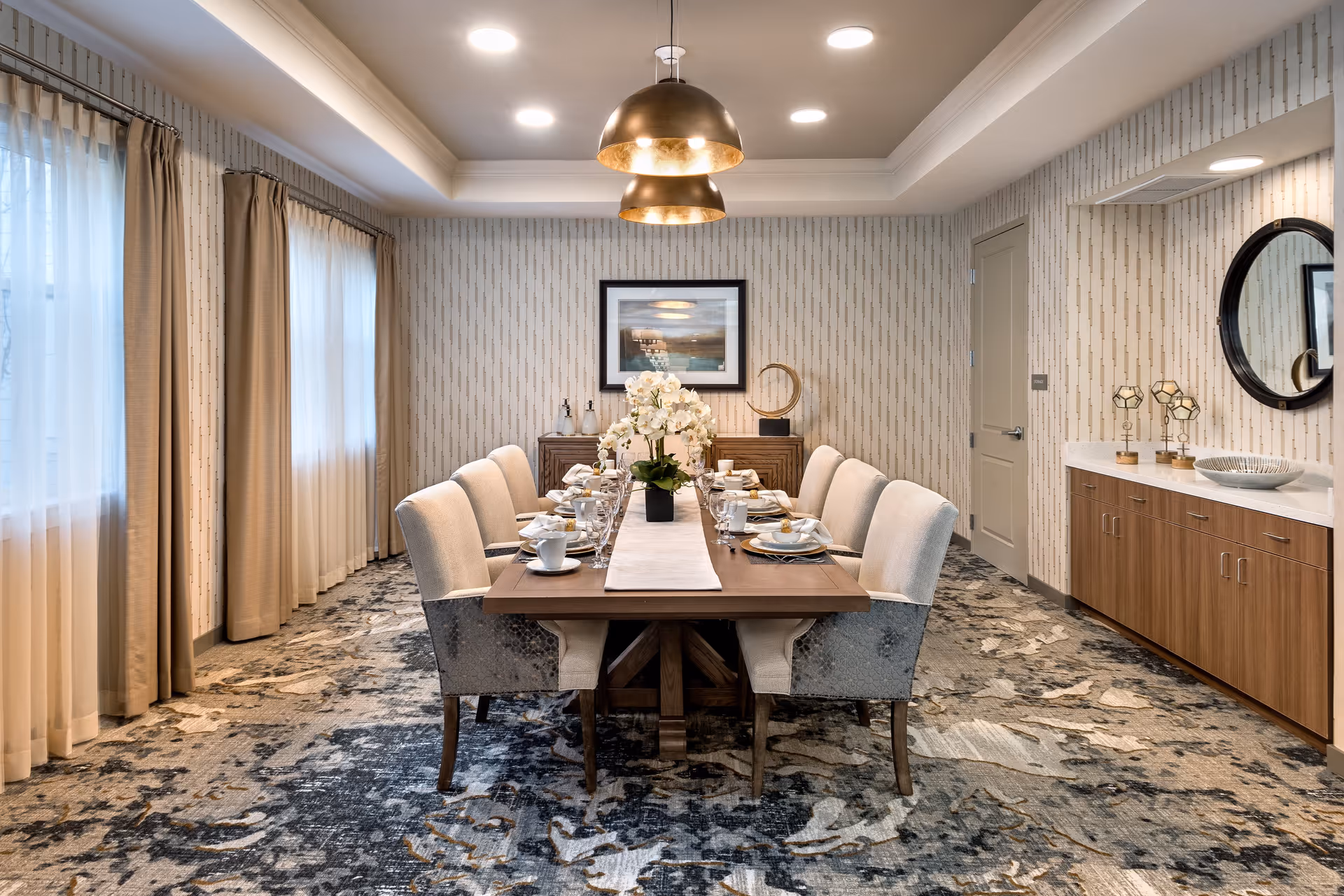 Elegant dining room with a long table set for a meal, upholstered chairs, pendant lights, and a sideboard.