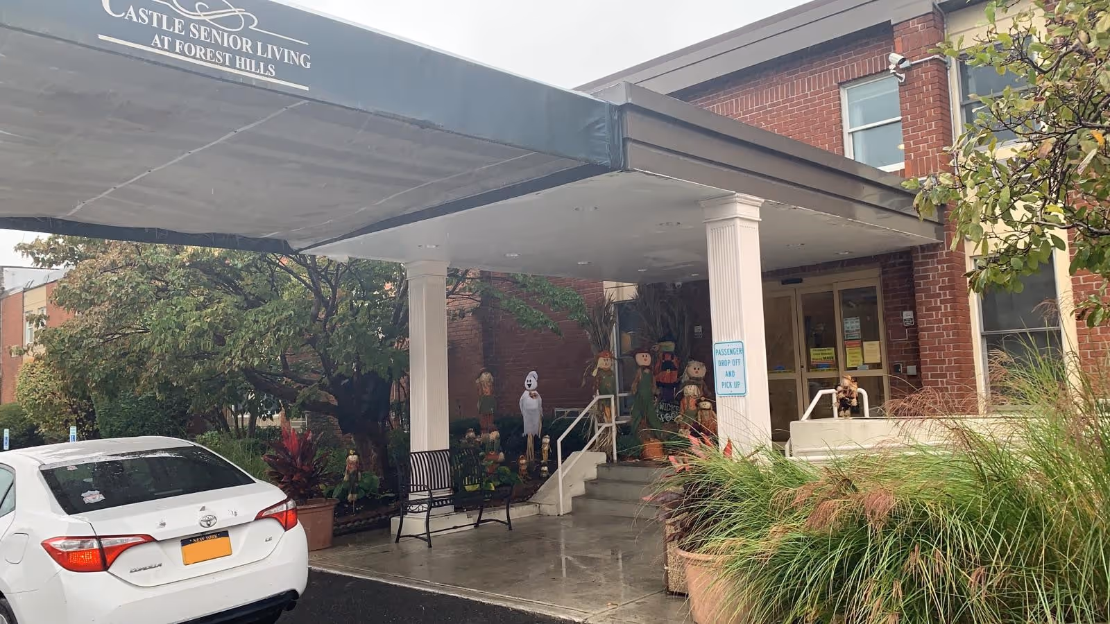 Front entrance of Castle Senior Living with a covered drop-off, parked car, and seasonal decorations.