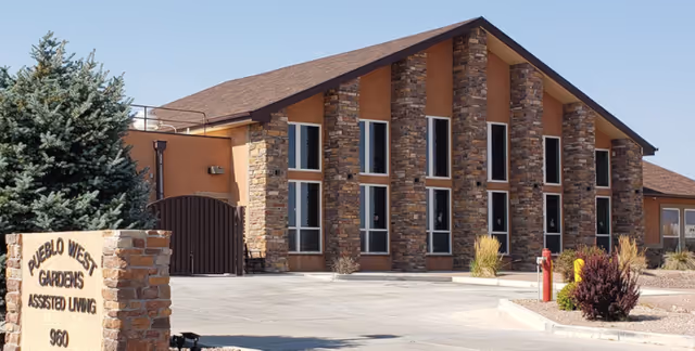 Exterior view of Pueblo West Gardens Assisted Living facility showing a building with stone and stucco facade, multiple tall windows, and a sign in front that reads 'Pueblo West Gardens Assisted Living 960'.