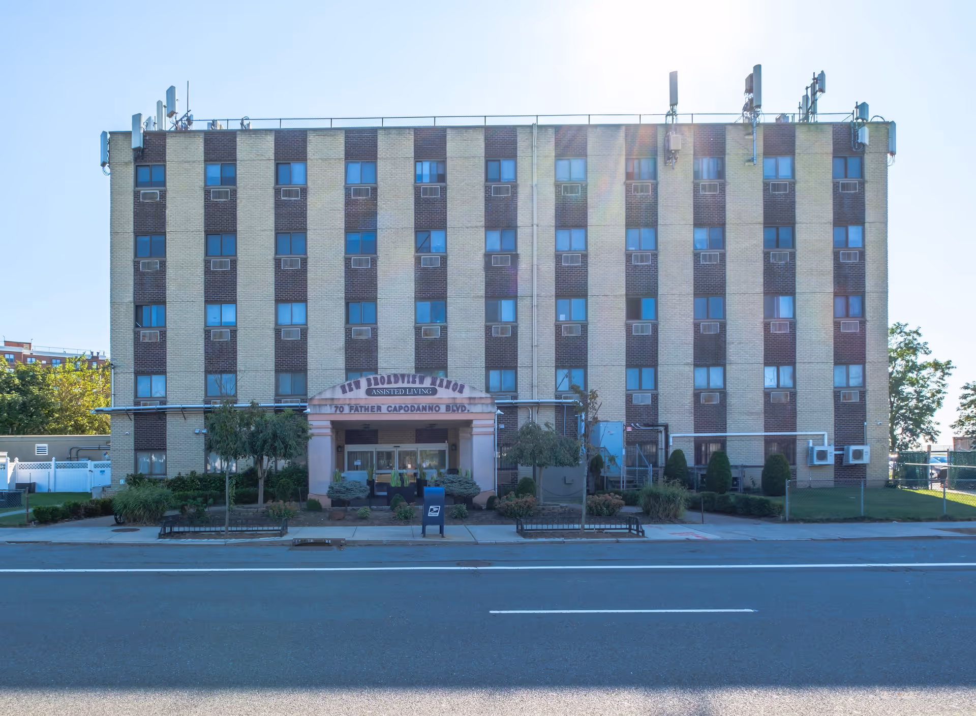 Front exterior view of New Broadview Manor, a multi-story assisted living building with a beige and brown brick facade, multiple windows with air conditioning units, and a covered entrance with the facility name and address displayed above.