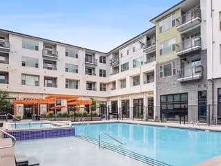 Outdoor courtyard featuring a swimming pool and spa surrounded by a multi-story senior living building with balconies and a pergola.