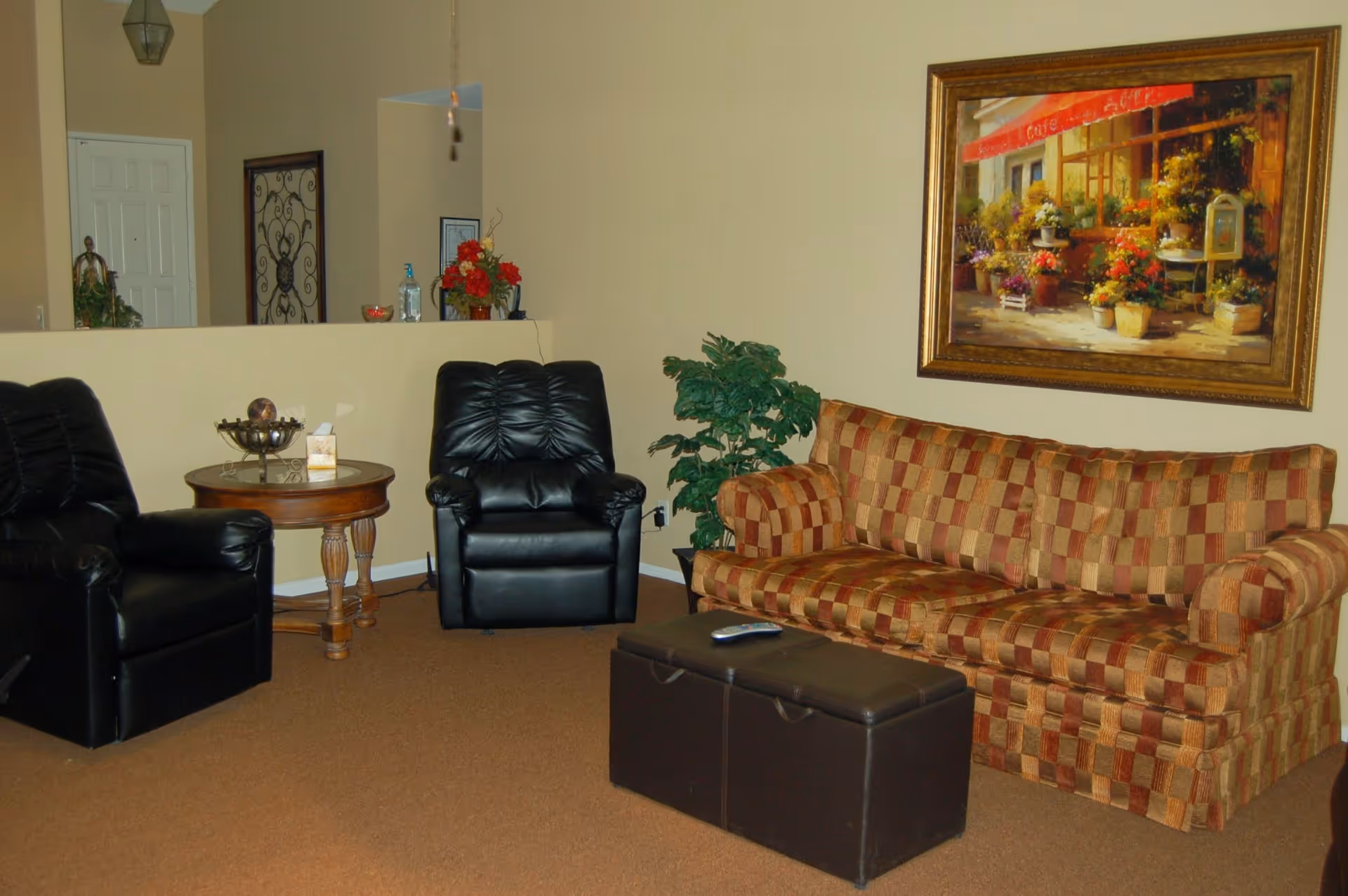 A cozy lounge area with a patterned sofa, black leather chairs, a dark coffee ottoman, and a framed painting on the wall.