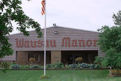 Front exterior of Wausau Manor Health Services with landscaping and flag.