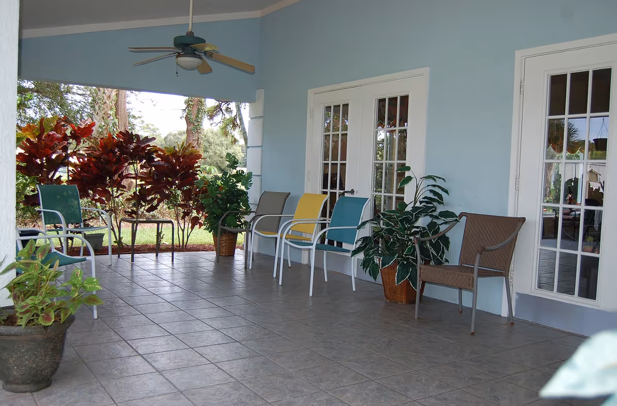 Covered outdoor patio with chairs, potted plants, a ceiling fan, and French doors.
