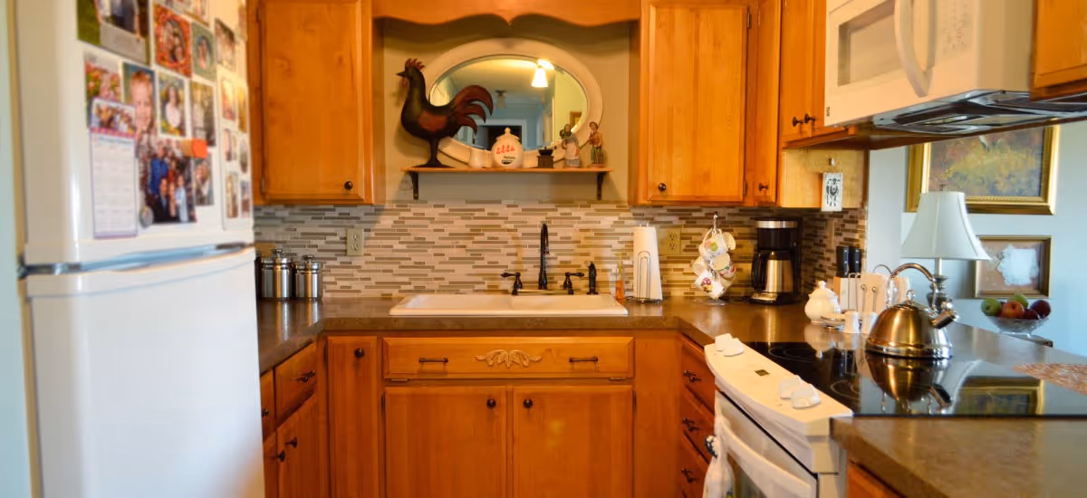 Compact kitchen with wooden cabinets, a sink under a decorative shelf, stove and microwave, refrigerator, and countertop appliances.