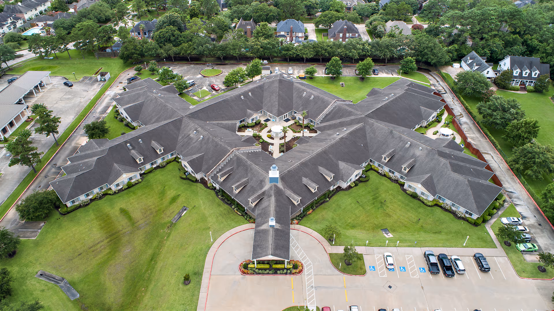 Aerial view of a star-shaped single-story senior living complex surrounded by lawns, driveways, and parked cars.
