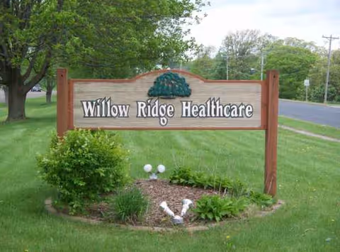 Wooden Willow Ridge Healthcare sign on a grassy landscape beside a road.