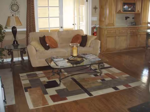 Cozy living room with beige sofa, glass coffee table, rug, and wooden cabinetry.
