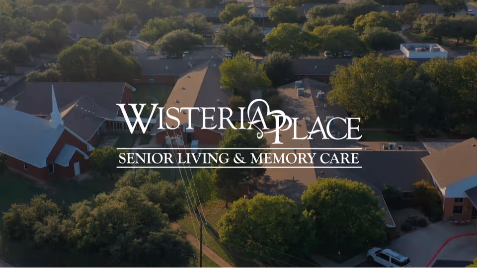Aerial view of a senior living campus with the overlaid text "Wisteria Place Senior Living & Memory Care".