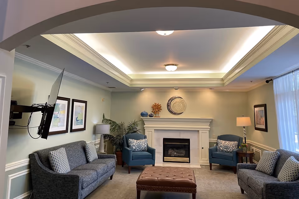 Well-lit common living room with sofas and armchairs arranged around a central fireplace and wall-mounted TV.