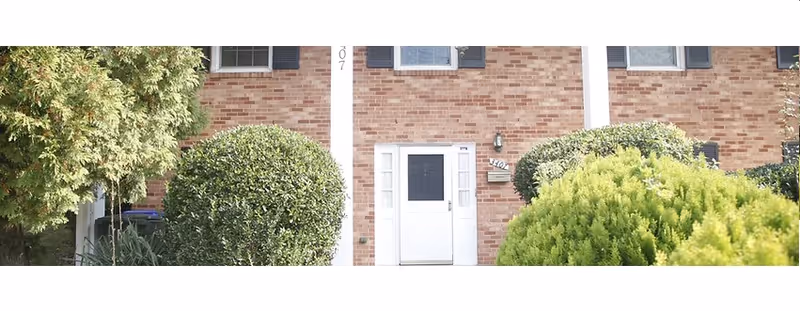 Brick building entrance with white door and manicured shrubs in front.