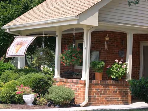 Brick building entrance with a covered porch, hanging plants, and flowering pots.