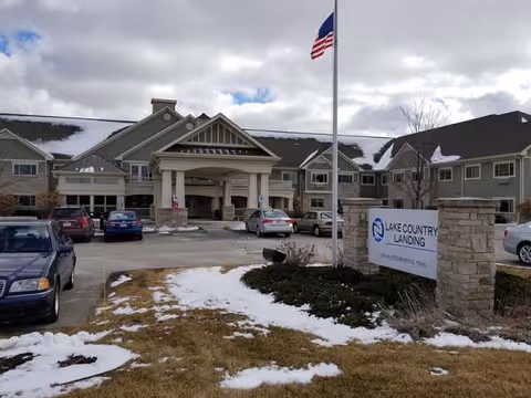 Exterior view of Lake Country Landing with entrance portico, flag, and parked cars.