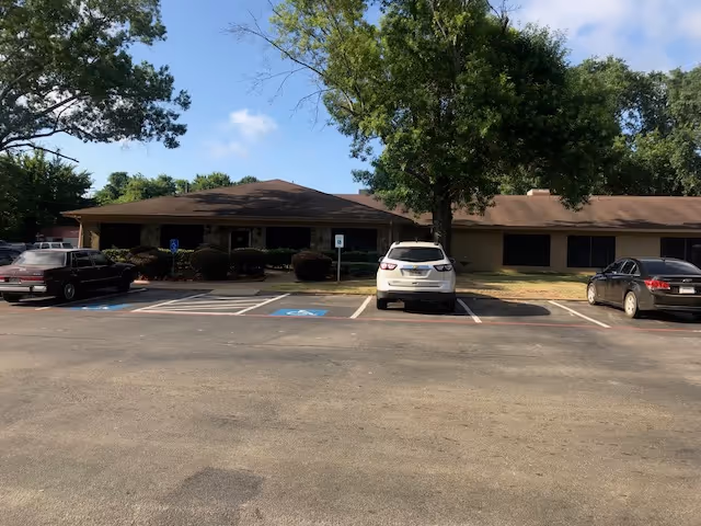 Front view of a single-story senior living facility with a parking lot and trees.