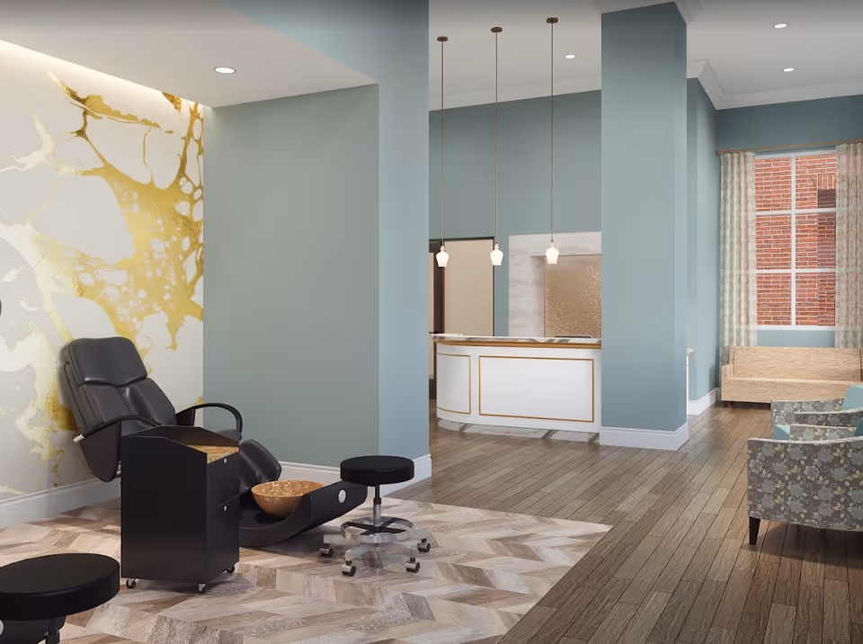 A modern interior space featuring a black reclining chair with a foot basin, two black stools on wheels, and a black rolling cart. The walls are painted light blue with a decorative gold and white accent wall. In the background, there is a white reception desk with gold trim, three pendant lights hanging from the ceiling, a window with patterned curtains, and several upholstered chairs and a beige sofa.