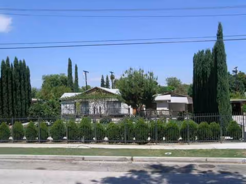 Exterior view of a single-story senior facility behind a fence with tall trees.