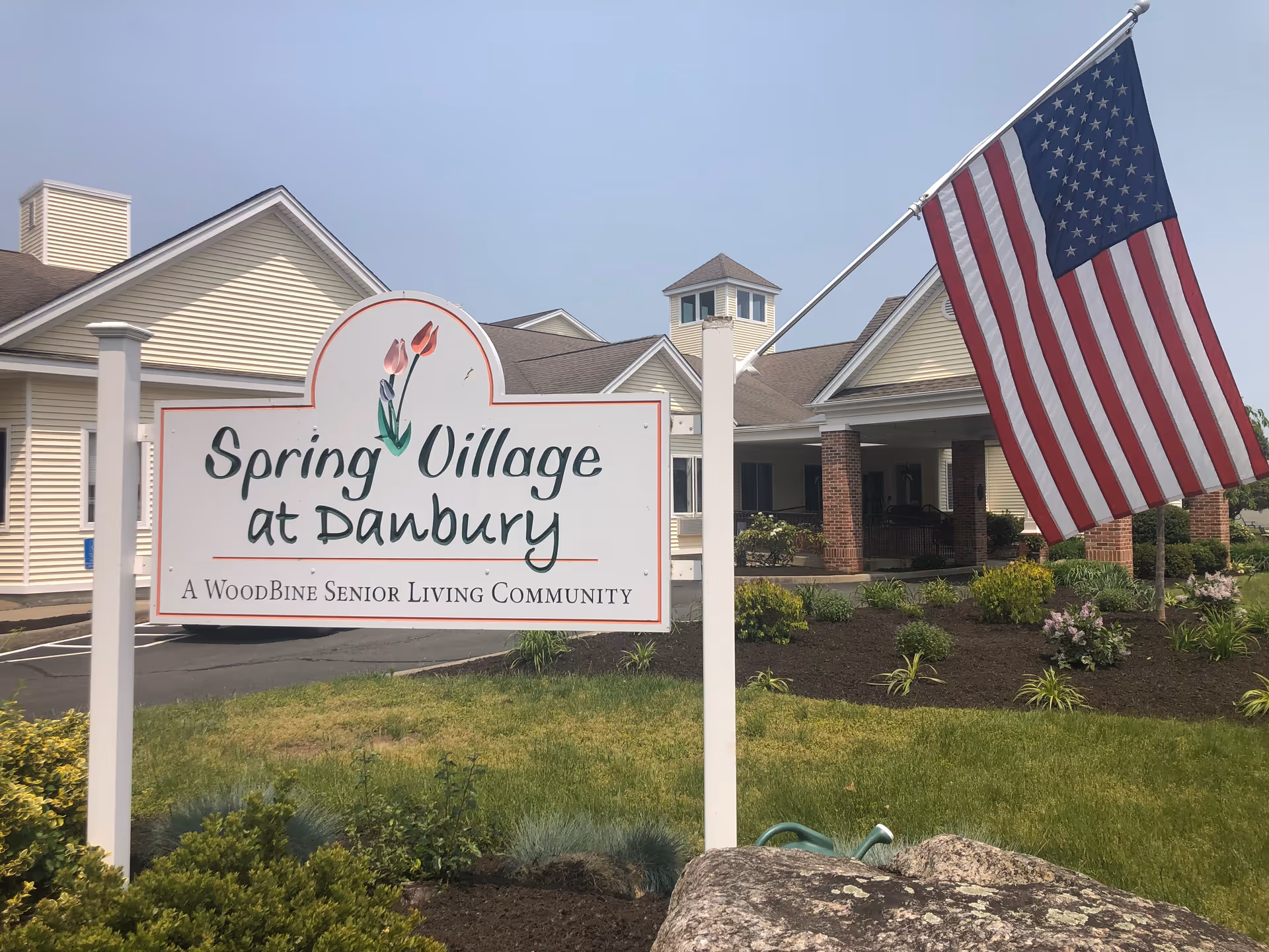 Front exterior of Spring Village at Danbury with a large sign and American flag.
