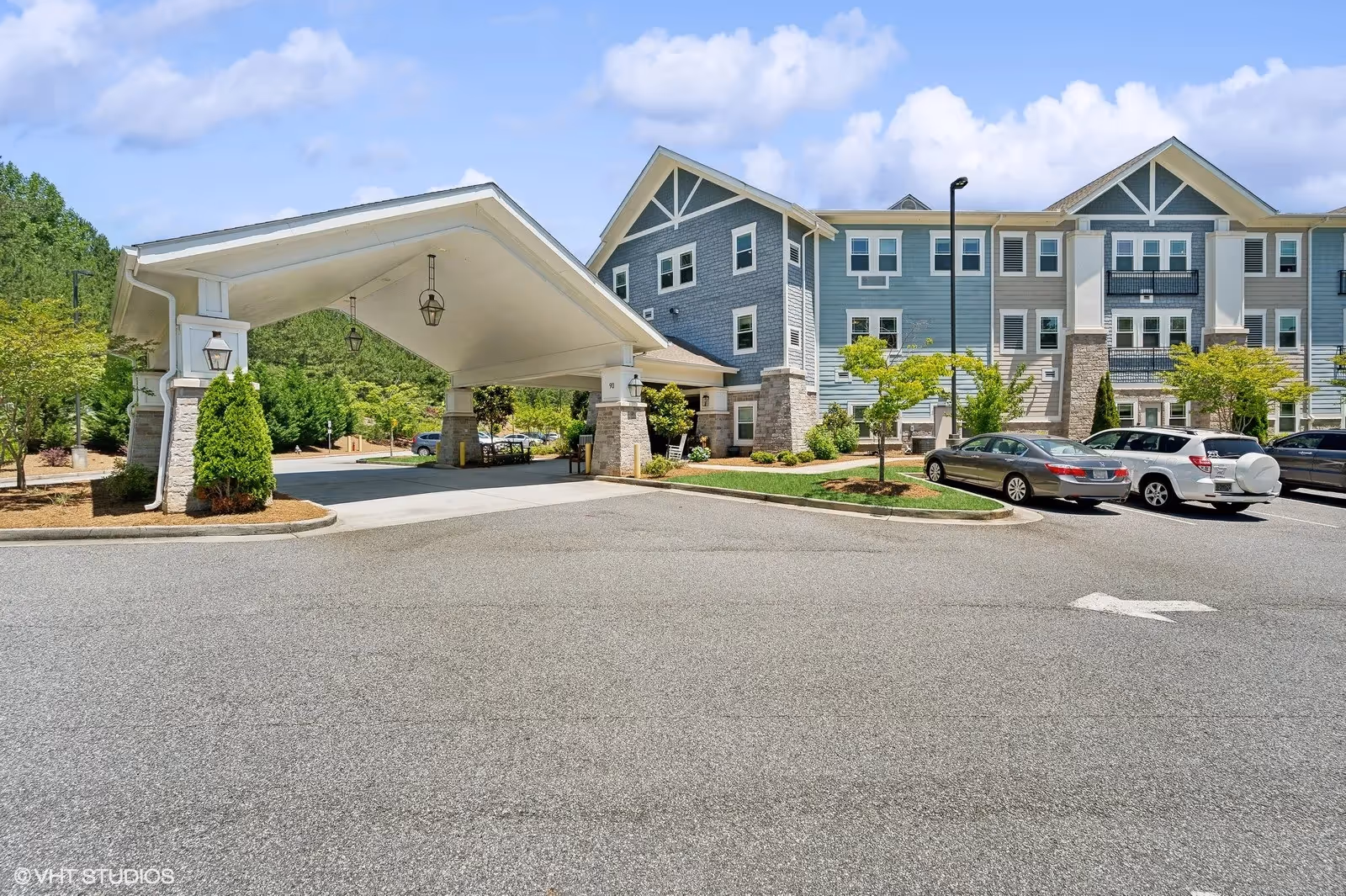 Covered entrance driveway and parking in front of a multi-story blue-sided senior living building.